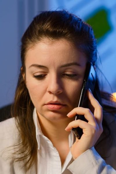Tired freelancer woman having conversation on phone while working exhausted in business office late at night doing overtime. Focused employee using modern technology network wireless overworking